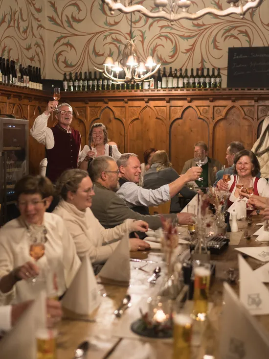 Group of people in traditional attire toasting at a festive dinner in a rustic wine tavern