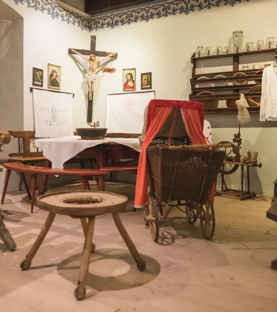 Stanza storica con culla d'epoca, arcolaio, crocifisso e oggetti domestici tradizionali