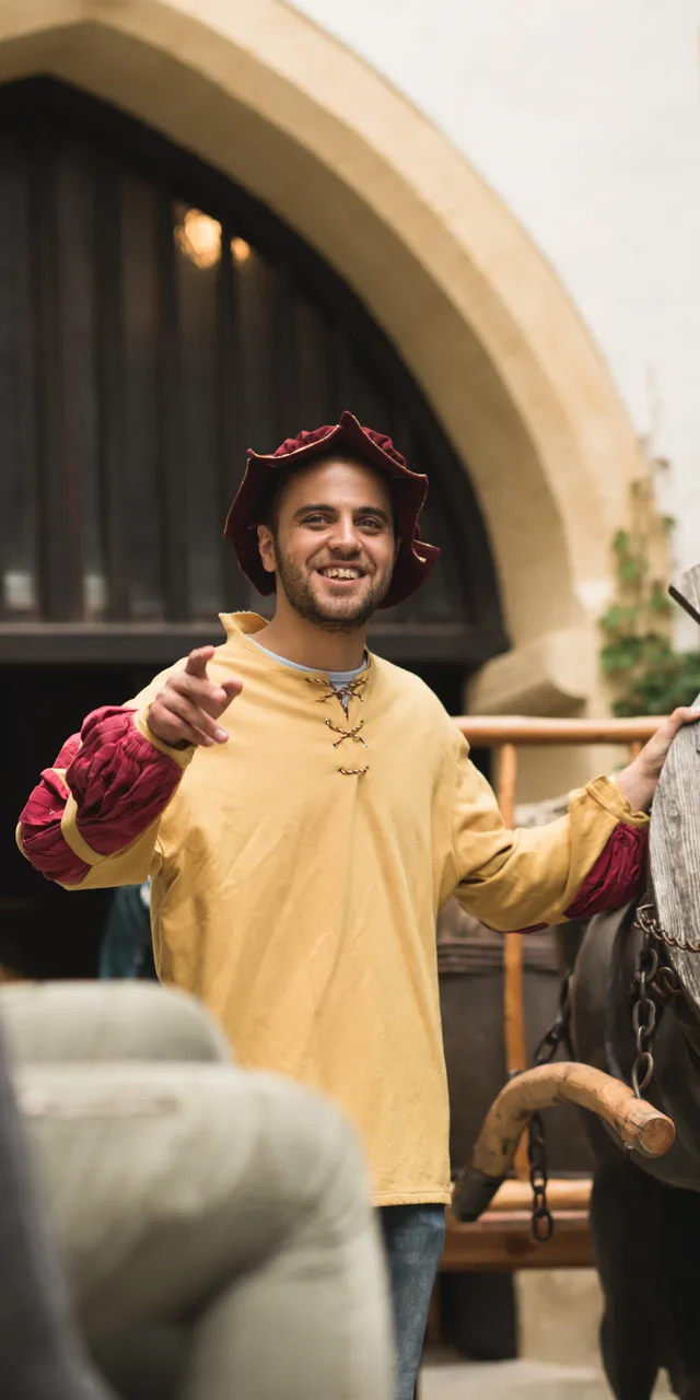 Rievocatore medievale guida visitatori accanto a un cavallo di legno in un cortile storico