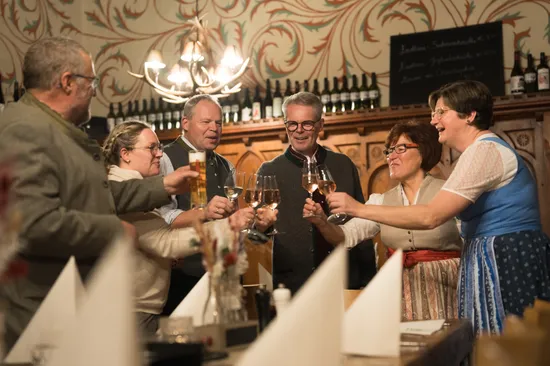 Group of people in traditional clothing toasting with wine and beer in a cozy restaurant