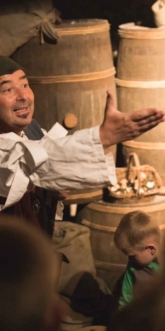 Historischer Darsteller erklärt einer Gruppe von Kindern und Erwachsenen ein mittelalterliches Lager