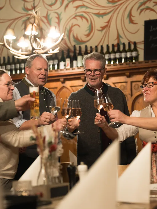 Gruppo di persone in abiti tradizionali brinda con vino e birra in un ristorante accogliente