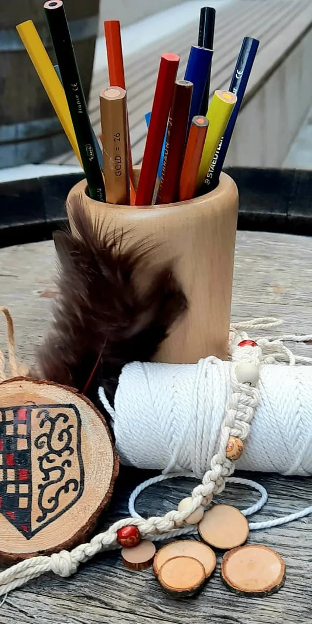 Rustikale Bastelmaterialien mit Buntstiften, Kordel, Holzmedaillon und Feder auf Holzfass