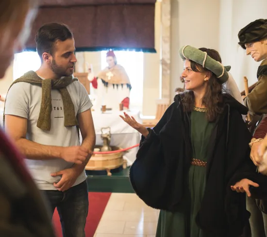 Turista interagisce con guida in costume in una mostra museale medievale con manichini