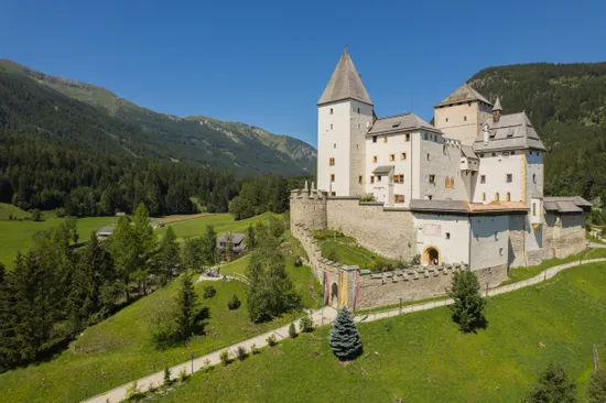 Weißes mittelalterliches Schloss in den österreichischen Alpen umgeben von grünen Hügeln und Wald