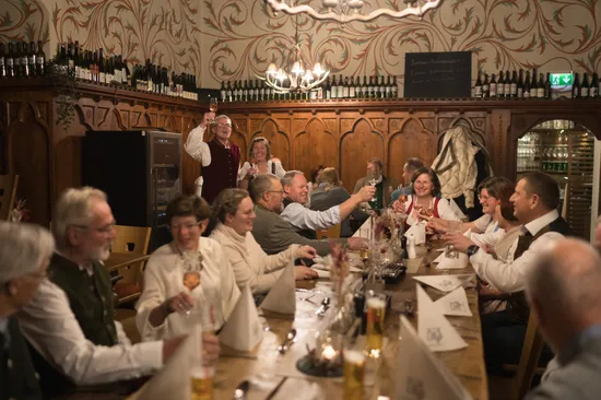 Group of people in traditional attire toasting at a festive dinner in a rustic wine tavern