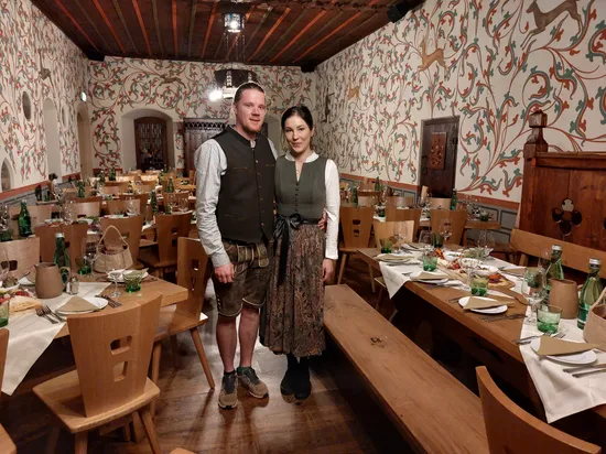 Couple in traditional Bavarian clothing standing in decorated dining hall set for dinner