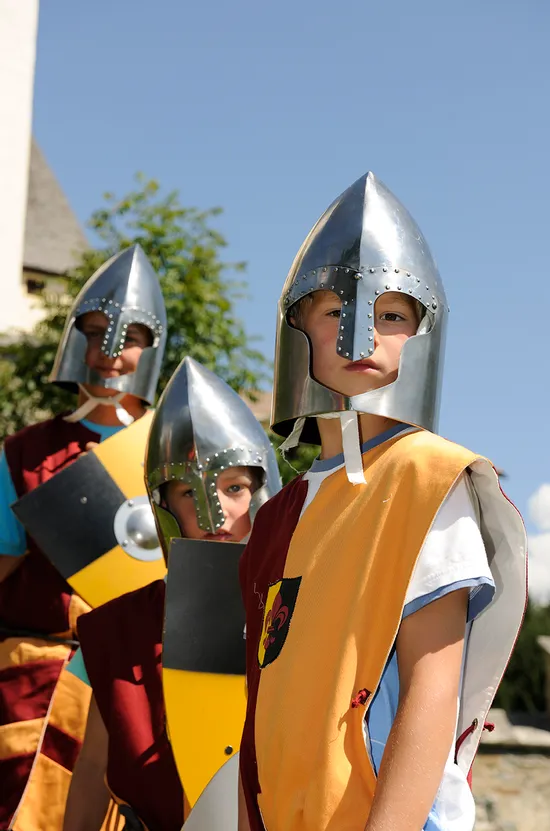 Kinder in mittelalterlichen Ritterkostümen mit Helmen und Schilden bei einer historischen Nachstellung