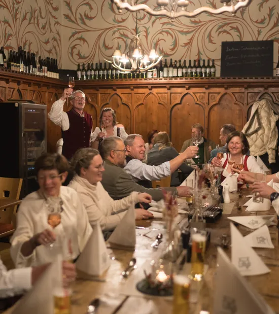 Group of people in traditional attire toasting at a festive dinner in a rustic wine tavern