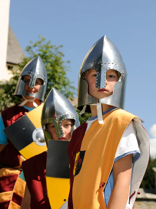 Kinder in mittelalterlichen Ritterkostümen mit Helmen und Schilden bei einer historischen Nachstellung