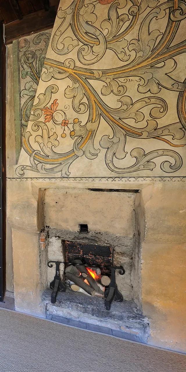 Stanza storica con scena di bagno medievale, affreschi murali e camino acceso