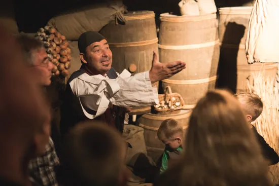 Historischer Darsteller erklärt einer Gruppe von Kindern und Erwachsenen ein mittelalterliches Lager