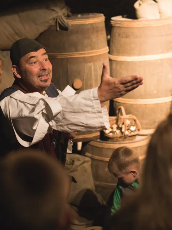 Historischer Darsteller erklärt einer Gruppe von Kindern und Erwachsenen ein mittelalterliches Lager